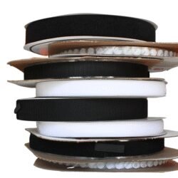 Pilas de rollos de Velcro con Adhesivo en colores blanco y negro, de diferentes anchos, destacando la variedad de opciones disponibles para proyectos.
