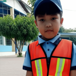 Niño usando un chaleco de Malla Infantil naranja con reflejantes, mostrando el uso práctico del chaleco de seguridad para niños en entornos escolares o públicos.